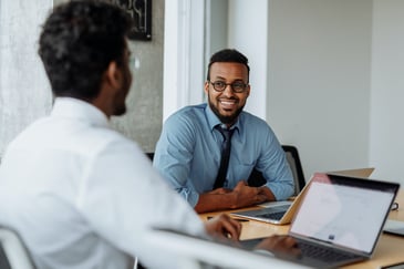 A manager and employee sitting at a desk smiling as the manager gives effective feedback to the employee. 