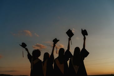 A group of five graduates waving their graduation caps in the air as they celebrate starting a new graduate training programme. 