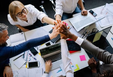 Five colleagues sharing a high five over a meeting room table as they agree to change their organisation's culture for the better. 