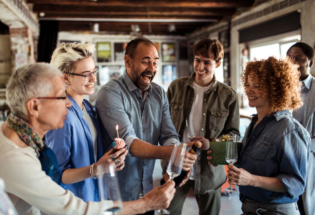 A group of five colleagues at work celebrating the new year with a bottle of champagne as they create a positive workplace after resolving any workplace conflicts before the start of the new year, and not letting anything go unsaid.