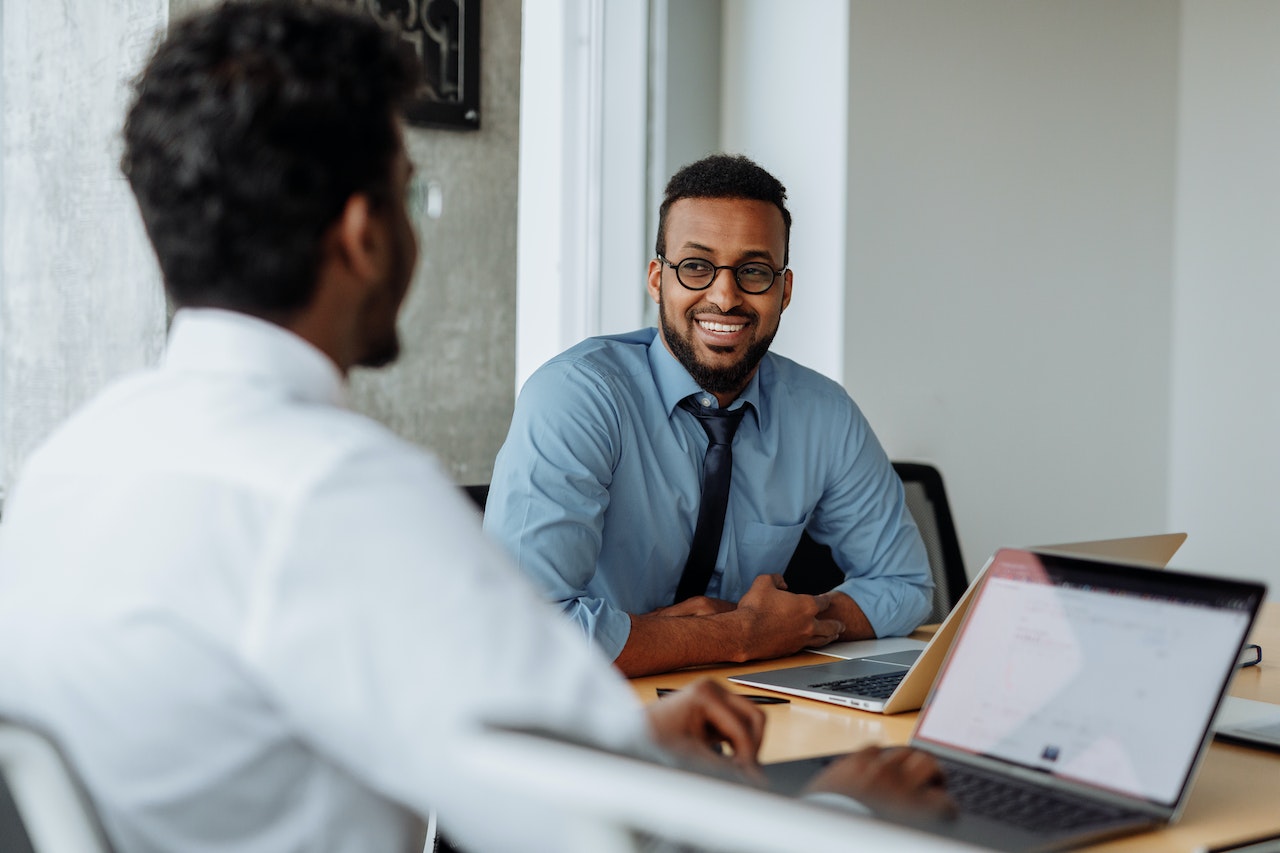 A manager and employee sitting at a desk smiling as the manager gives effective feedback to the employee.