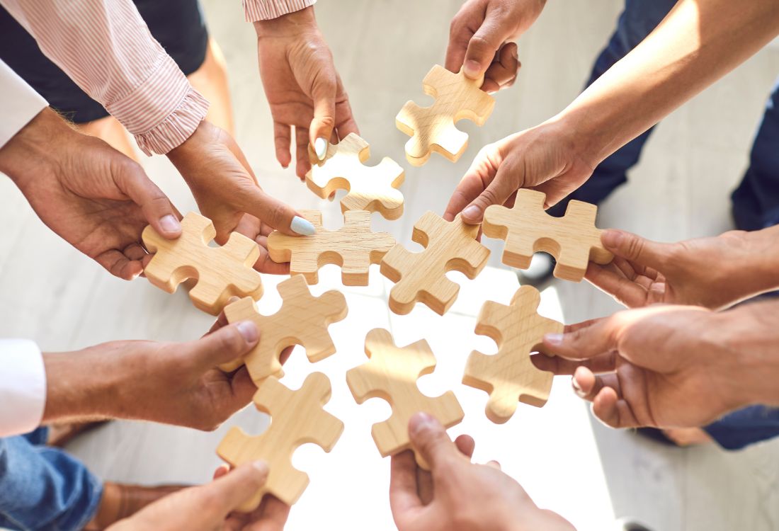 A team of colleagues working together to connect large puzzle pieces in a business simulation to help improve and impact their organisational results.