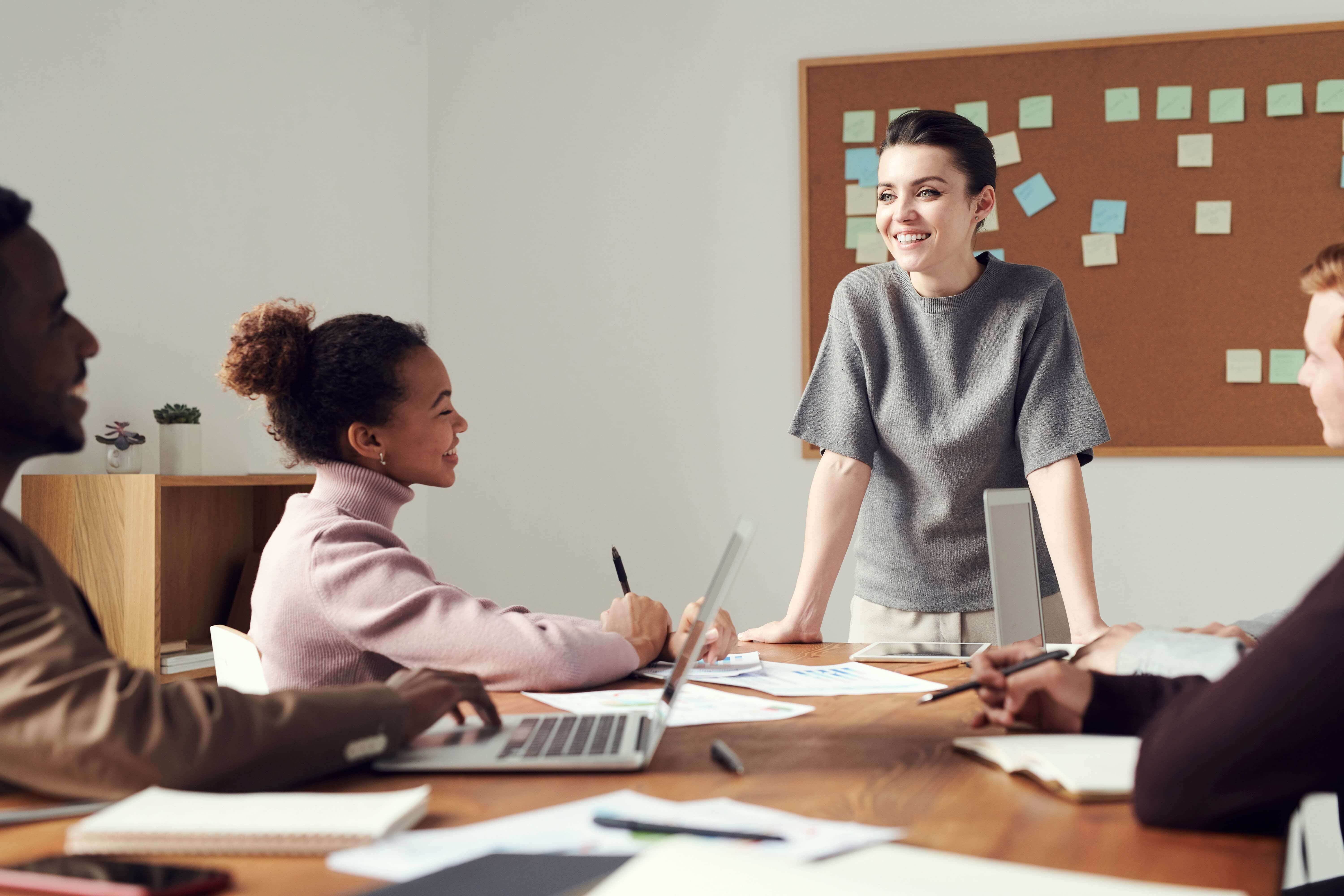 A woman smiling and standing in front of graduates, training them on how to succeed in their career, which will help the longevity of their business. 