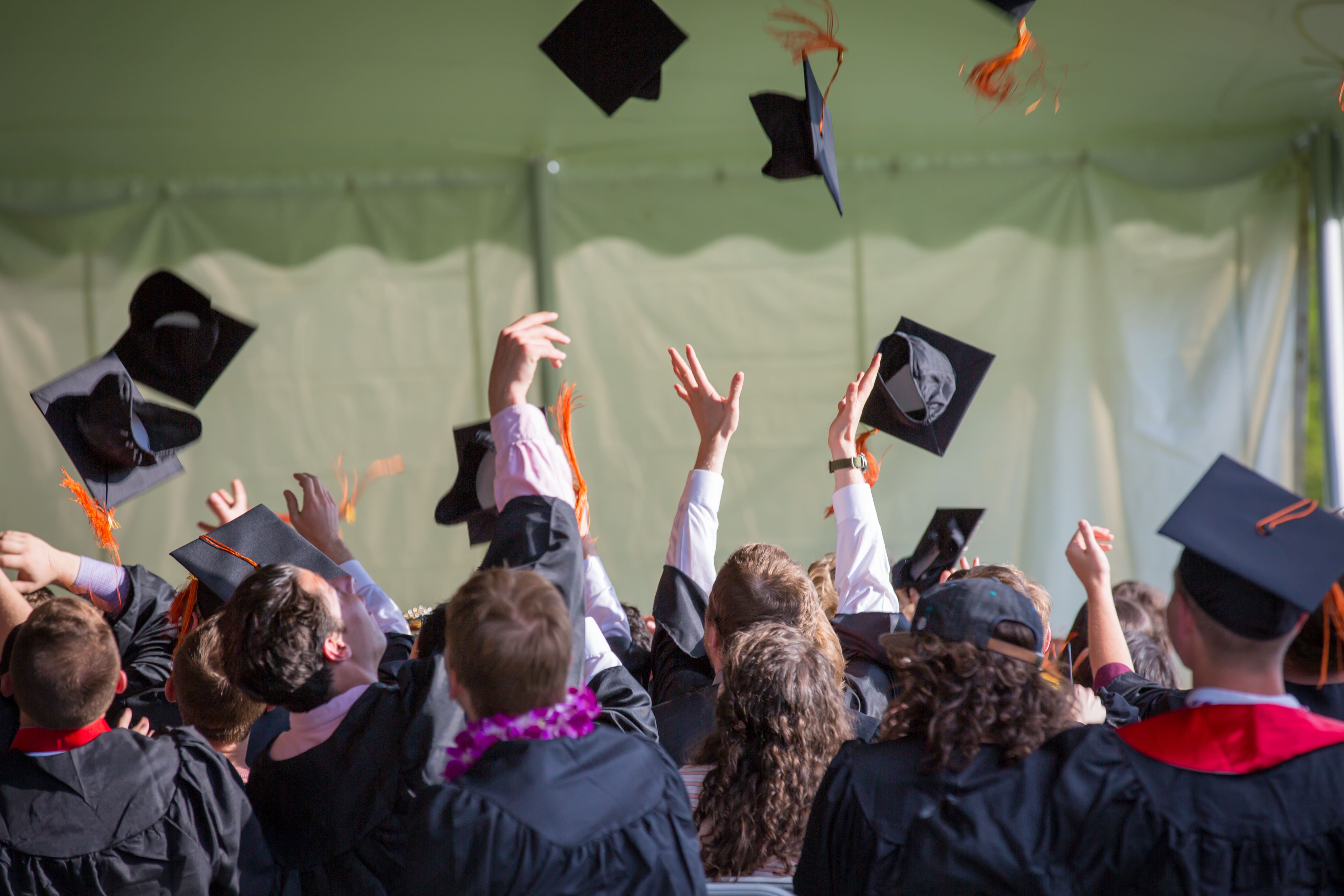 Graduates throwing their mortarboards into the air, knowing they’ll provide a great ROI for companies that recruit graduates. 