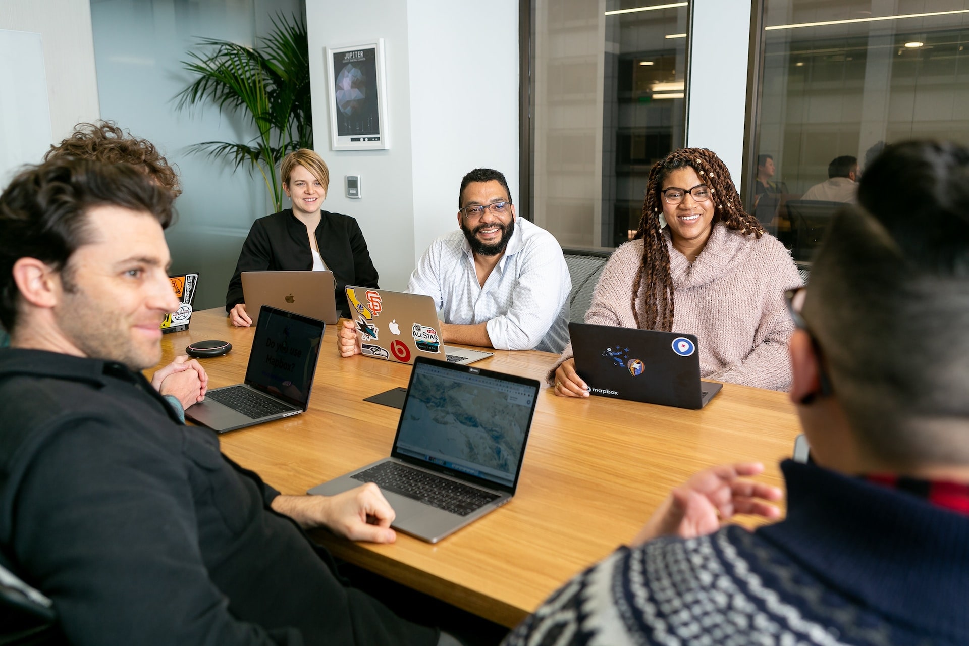 Five managers sitting around the table in a meeting room with laptops open in front of them as they have a productive and effective leadership team meeting.