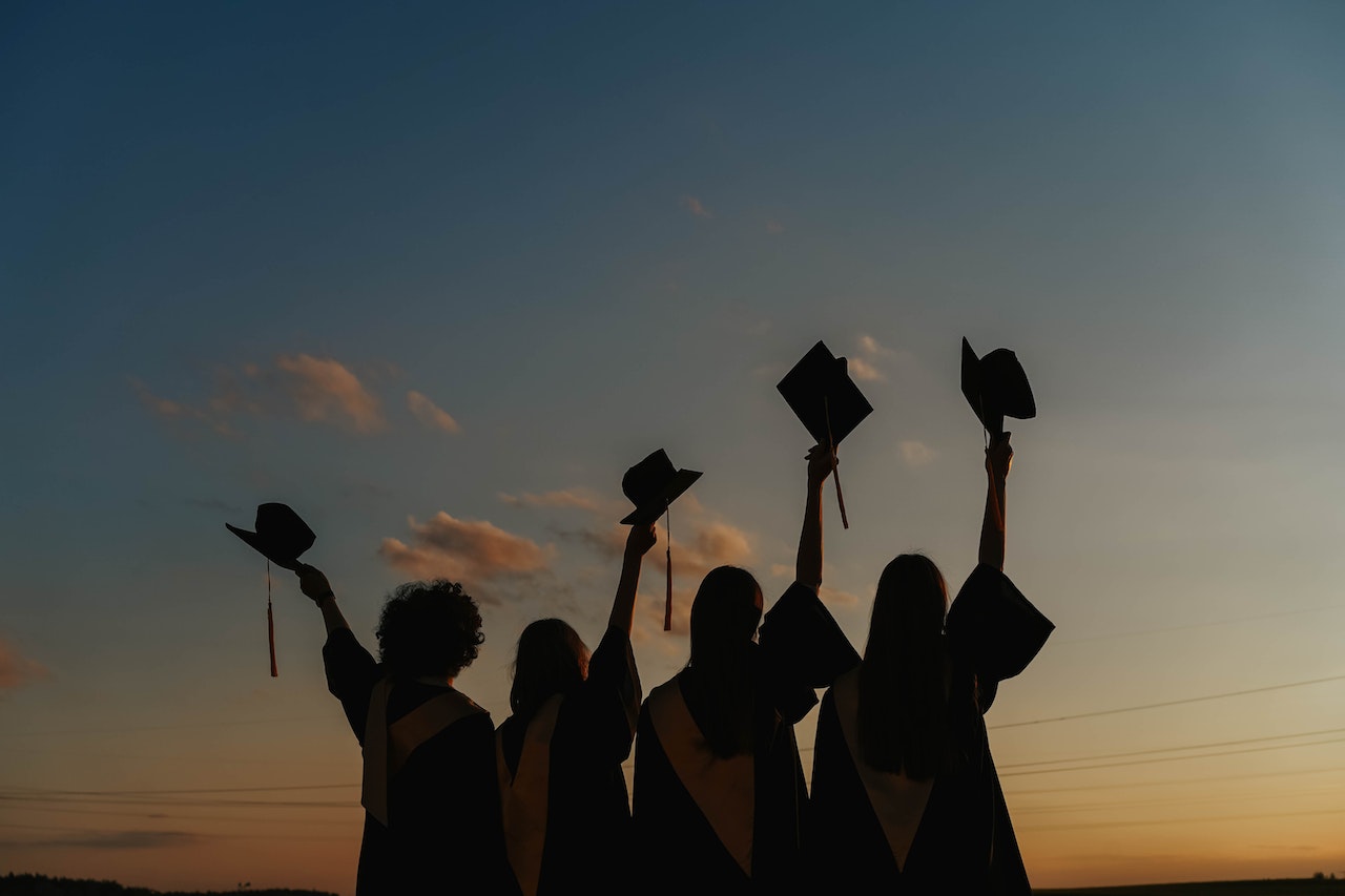 A group of five graduates waving their graduation caps in the air as they celebrate starting a new graduate training programme.