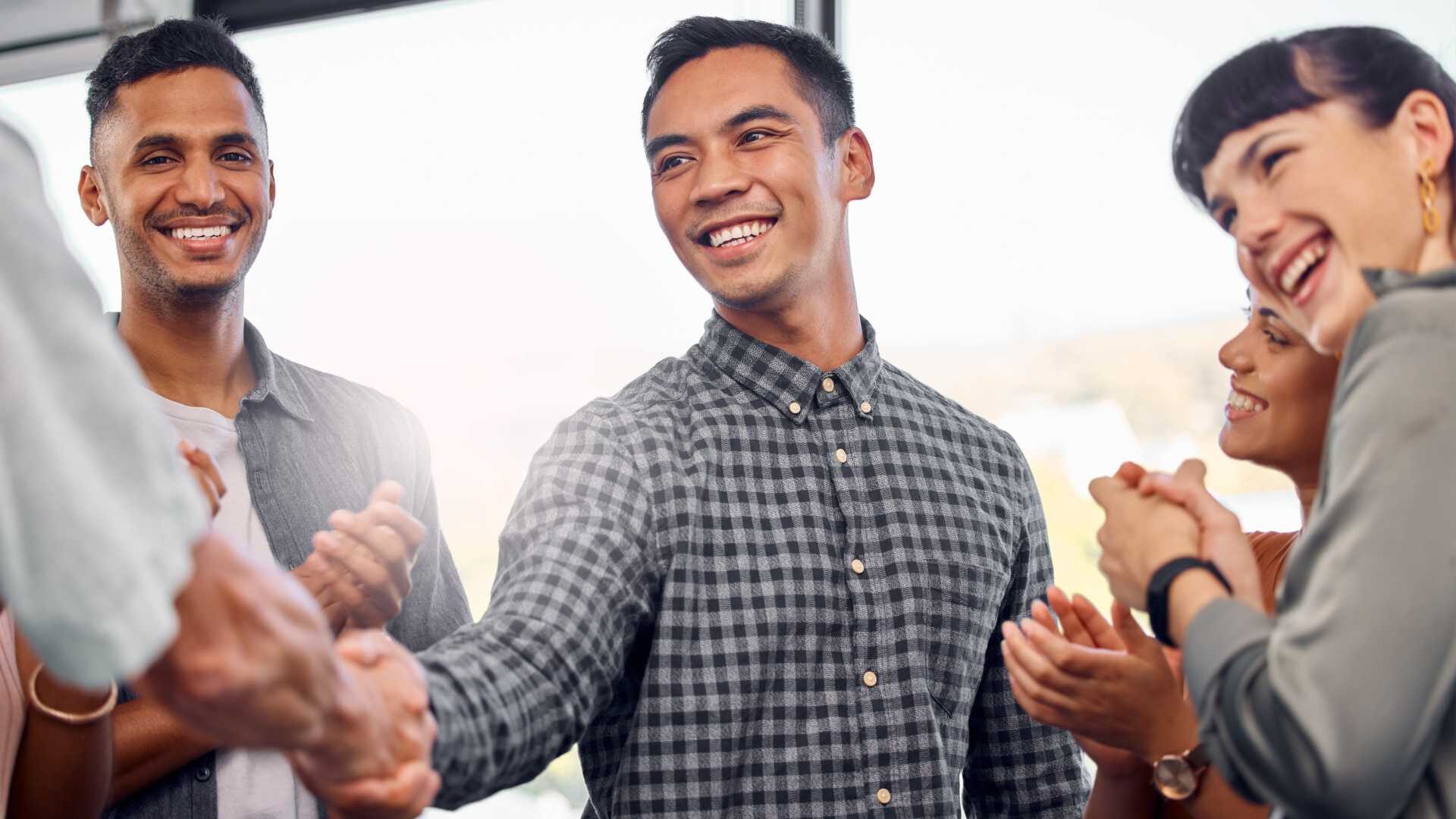 A group of smiling young professionals meeting and shaking hands with one of their own who is in a leadership position because of his resilience 