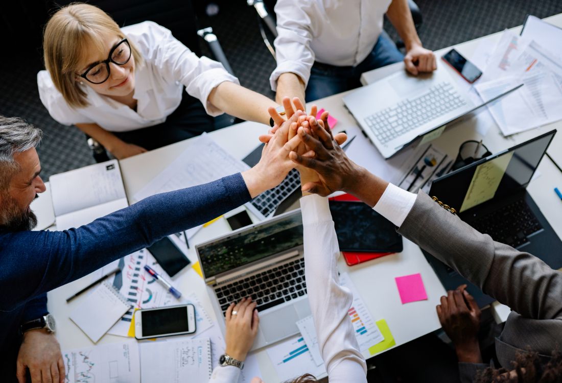 Five colleagues sharing a high five over a meeting room table as they agree to change their organisation's culture for the better.