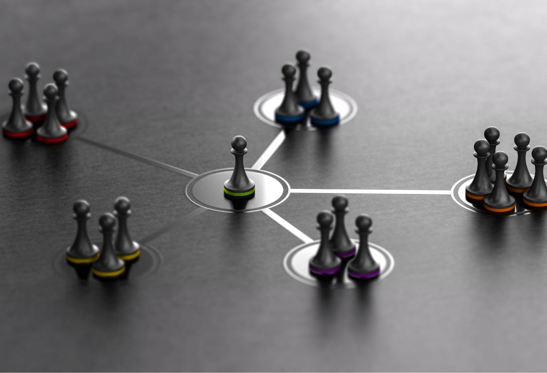 A central business owner pawn in the centre with five groups of pawns connecting to the central one which form a cohesive leadership team of a business that are aligned on their responsibilities and delegation of tasks.